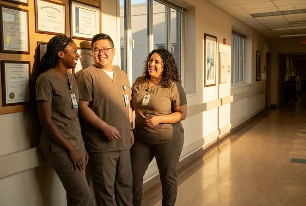 Three diverse nurses laughing together in hospital hallway