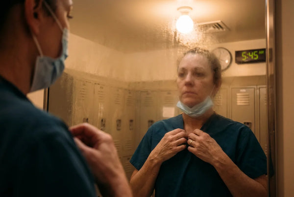 Nurse adjusting scrub collar in locker room mirror before shift
